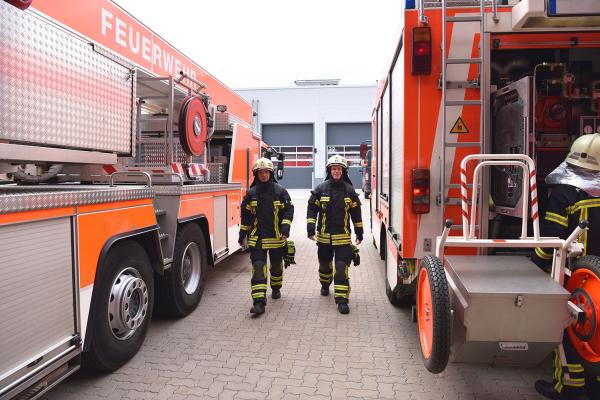 Two firefighters between two fire engines in front of a fire station